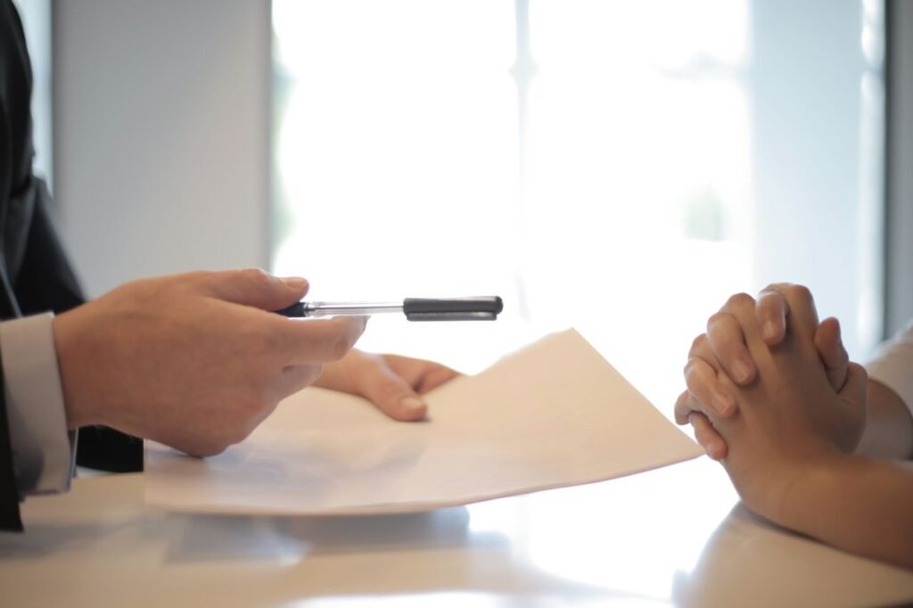 Side view of faceless formal man giving pen and paper to focused female with clenched hands at table on meeting